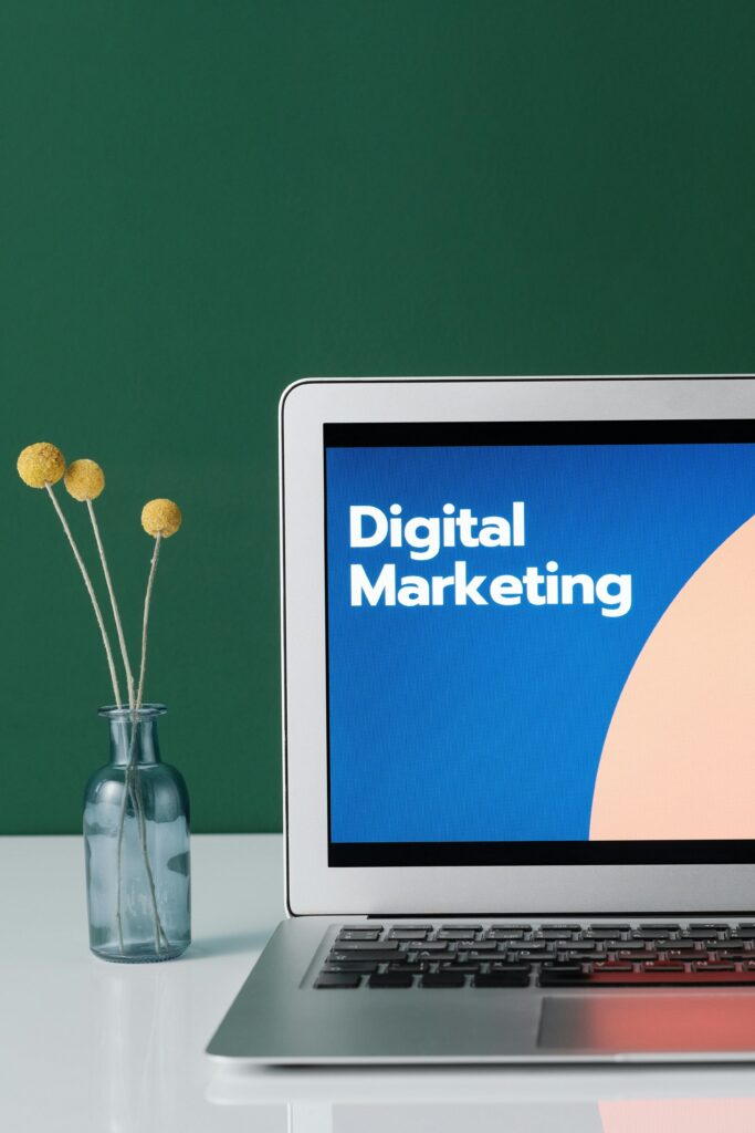 Modern laptop with the text 'Digital Marketing' on the screen, placed on a clean desk with a small vase of yellow flowers, representing Florya Bay Corporation's expertise in digital marketing and e-commerce