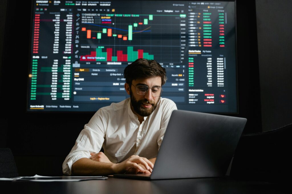 A professional analyzing data on a laptop with a trading dashboard in the background, symbolizing Florya Bay Corporation's innovative approach to global trade and digital marketing